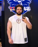 Modelo com Regata Muscle Oversized off-white, rosto e camiseta inteiros, centralizado no espelho com celular e fundo original